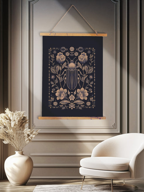 A symmetrical wall tapestry featuring a large scarab beetle in antique bronze tones surrounded by detailed flowers and botanical elements on a black background, mounted on wooden dowels with twine.